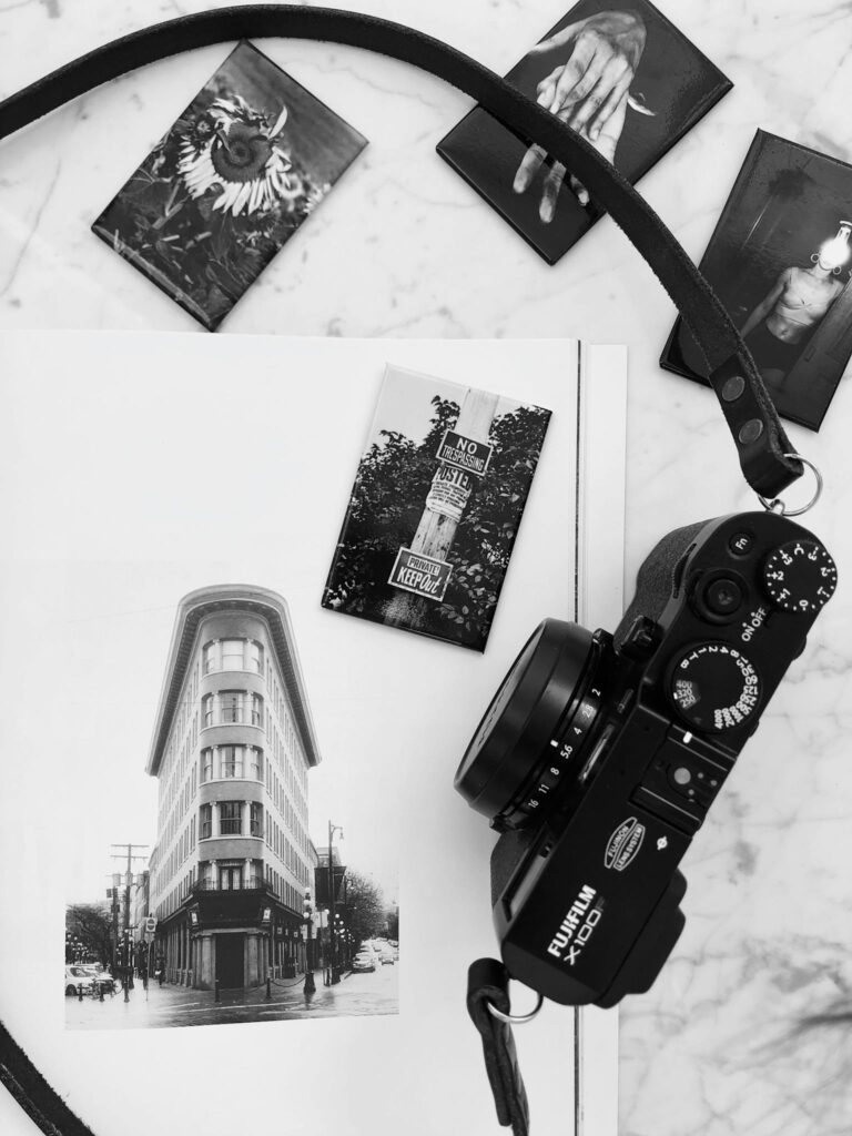 Black and white photo camera placed on white marble table near album with various photos in modern studio