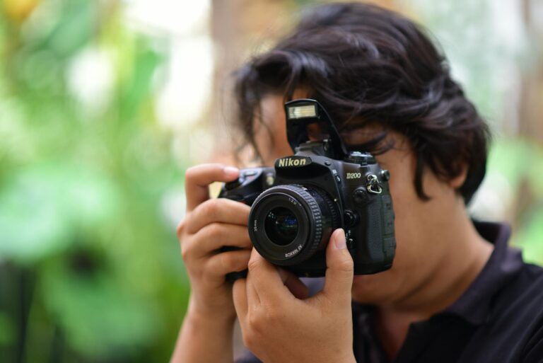 Close-up of a person using a DSLR camera outdoors with blurred green background.